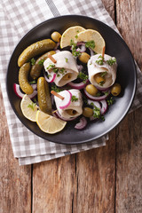 rolls of marinated herring with olives, onions, pickles and lemon close-up on a plate. Vertical top view