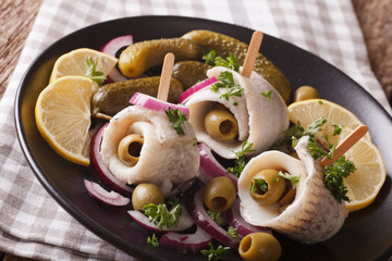 rolls of marinated herring with olives, onions, pickles and lemon close-up on a plate. Horizontal
