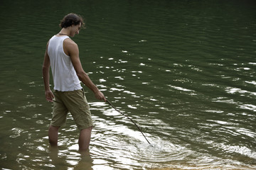 Young man standing in lake, playing with stick