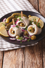 rolls of marinated herring with olives, onions, pickles and lemon close-up on a plate. vertical