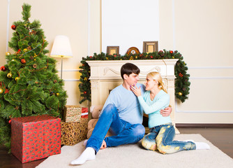 Nice love couple sitting on carpet near the fireplace. Woman and man celebrating Christmas