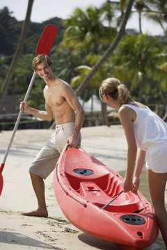 Couple Pulling Kayak Up Beach