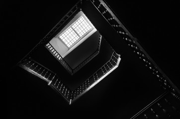 Obraz premium Outlines of the square staircase in building in low light with attic window. Bottom view