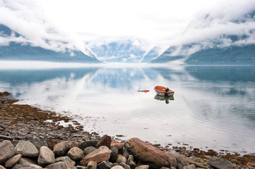 Morning by the fjords, clouds on the mountains with reflection on the water and small boat, Norway
