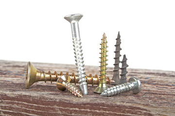 Various screws on old wooden plank on a white background