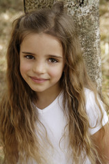 young girl leaning against tree trunk