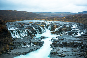 Bruarfoss or waterfall bridge, consists of numerous runlets falling into a chasm at the middle. At the chasm, the water of Bruara river is colored in glacial blue running on black volcanic bedrock.