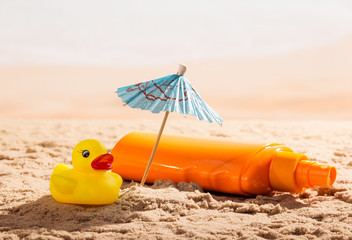 Fototapeta na wymiar Sunscreen, umbrella and rubber duck in the sand on seashore.