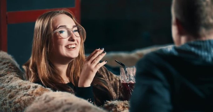 Young woman with beverage laughing with man at bar 4k video. Couple talking and sitting at cafe sofa, girl flirts with guy, smiling, back view