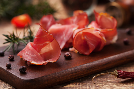 Delicious prosciutto ham on a wooden board with spices.