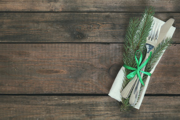 Country style christmas decoration with fir tree and green ribbon cutlery on old wooden brown background.