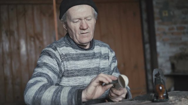 Happy wrinkled man hewing his handmade wooden spoon and smiling at camera 4K