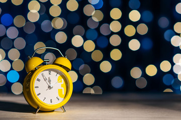 yellow classic alarm clock on a shimmering background, celebration atmosphere. Place for text - obrazy, fototapety, plakaty