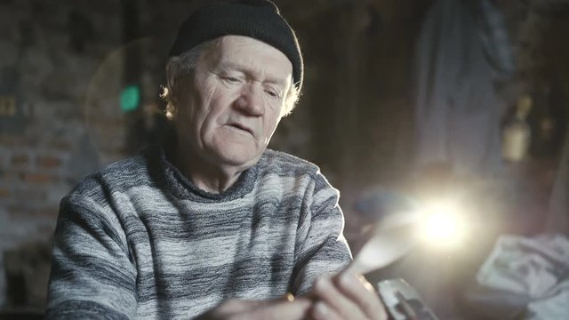 Old wrinkled carpenter showing handmade wooden spoon and smiling at camera 4K