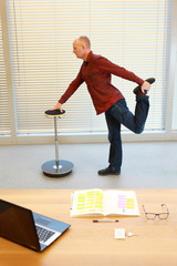 leg exercise durng office work - middle age  standing man stretching  on pneumatic stool in his...