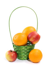 Натюрморт с апельсинами и яблоками в плетёной корзинке на белом фоне
