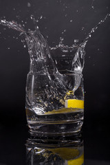 Falling in a glass of lemon, splash on black background, isolated, water drops