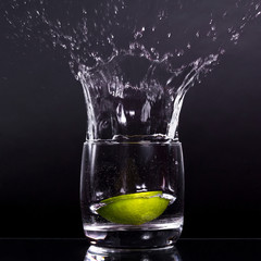 Falling in a glass of lemon, lime, splash on black background, isolated, water drop