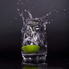 Falling in a glass of lemon, lime, splash on black background, isolated, water drop