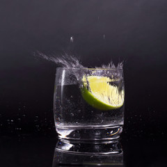 Falling in a glass of lemon, lime, splash on black background, isolated, water drop