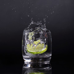 Falling in a glass of lemon, lime, splash on black background, isolated, water drop