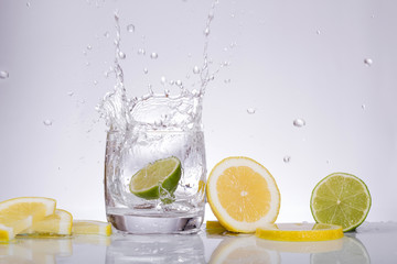 Fototapeta na wymiar Splashes of water, lemon lime falling into a glass, isolated, reflection, white background, water drop