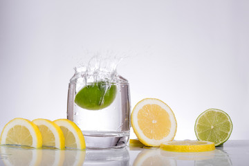Splashes of water, lemon lime falling into a glass, isolated, reflection, white background, water drop