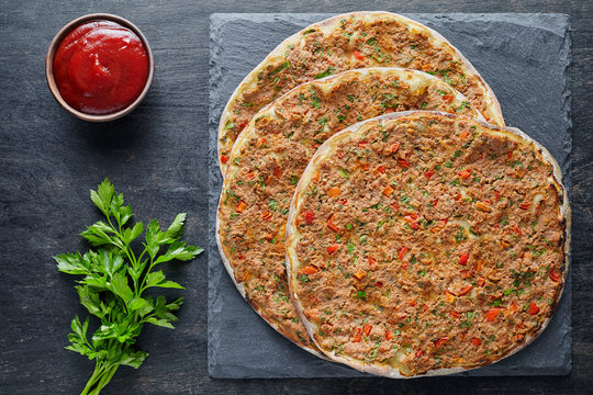 Lahmacun traditional turkish pizza with minced beef or lamb meat, paprika, tomatoes, cumin spice, parsley baked spicy middle eastern food on dark table background