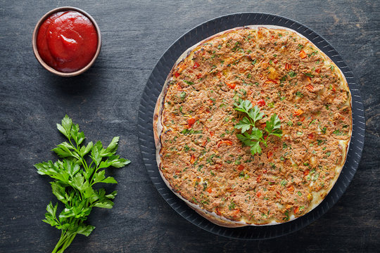 Lahmacun traditional turkish restaurant pizza with minced beef or lamb meat, paprika, tomatoes, cumin spice, parsley baked spicy middle eastern food on dark table background