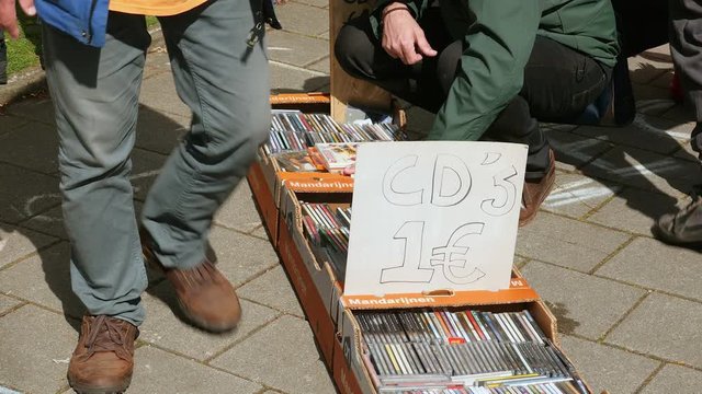 A sign reading CD's for sale and boxes of cd's on the pavement at yard sale.