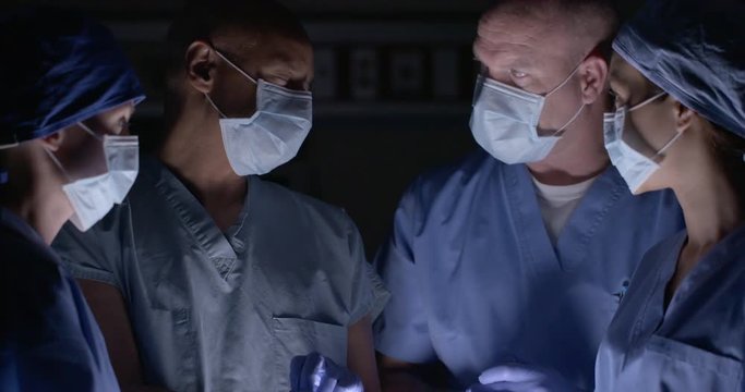 Surgical team of doctors and nurses in scrubs and masks, pull on rubber gloves and have discussion as they prepare for an operation.  Close up recorded at 60fps.