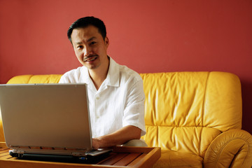 Man sitting on sofa, using laptop, looking at camera, portrait