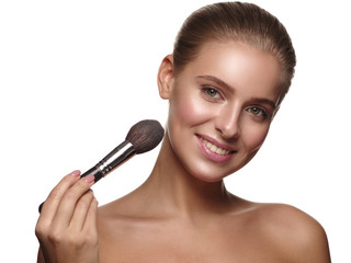 Portrait of a girl with pure and healthy glowing smooth skin, who is applying daily makeup on her face using a brush in her hand, studio shoot, white isolated background
