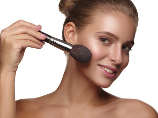 Portrait of a girl with pure and healthy glowing smooth skin, who is applying daily makeup on her face using a brush in her hand, studio shoot, white isolated background
