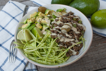 Green raw vegan zucchini pasta with lentils, pesto, tahini, avocado, olives and oil. Delicious food detox every day.