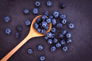  fresh picked blueberries in wooden spoon on black stone