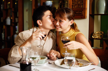 Couple in Chinese restaurant, holding wine glasses, man kissing woman on cheek