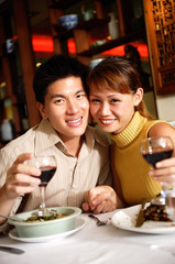 Couple in restaurant, smiling at camera, holding wine glasses