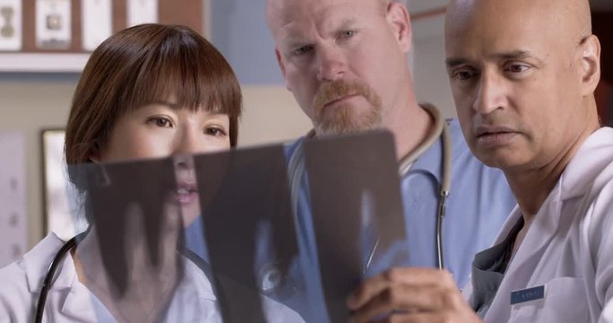 Male nurse and two doctors consult with each other while looking at X ray photograph in hospital exam room.  Close up with nurse center.