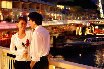 Couple standing next to railing, woman holding rose