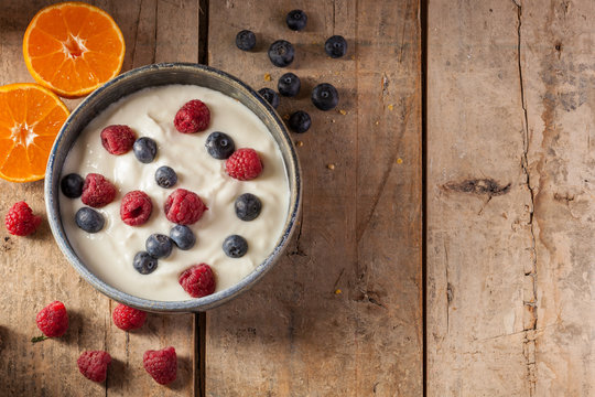 Healthy organic breakfast with greek yogurt, raspberries, blueberries, muesli, tangerine, bread and cheese. On a rustic wooden table. With copy space.