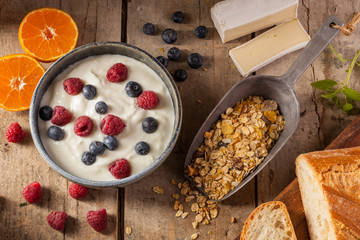 Healthy organic breakfast with greek yogurt, raspberries, blueberries, muesli, tangerine, bread and cheese. On a rustic wooden table.