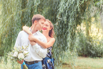 Naklejka premium Happy young couple, she hugs him from behind. Holding a bouquet.