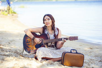 young beautiful woman playing a guitar while sitting on the sand