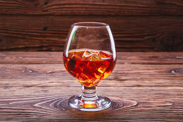 whiskey cognac with ice cubes in a glass on a wooden background