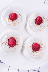 Group of meringue nests topped with whipped cream and raspberry