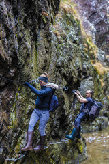 couple of hikers climbing on safety cables in a gorge above the