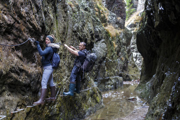 couple of hikers climbing on safety cables in a gorge above the