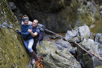 couple of hikers climbing on safety cables in a gorge above the