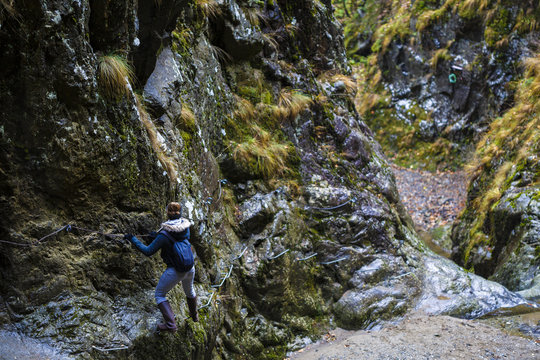 Woman Hiker Climbing On Safety Chains Through A Very Narrow Gorg